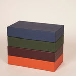 Four booklet leather backgammon sets stacked in navy, olive green, taupe and orange