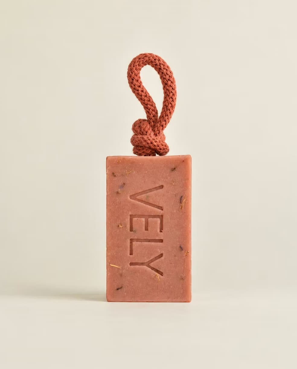 A rectangular terracotta-colored soap bar with the brand name 'VELY' embossed vertically, featuring a matching braided cord loop at the top, set against a plain light beige background.