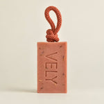 A rectangular terracotta-colored soap bar with the brand name 'VELY' embossed vertically, featuring a matching braided cord loop at the top, set against a plain light beige background.