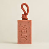 A rectangular terracotta-colored soap bar with the brand name 'VELY' embossed vertically, featuring a matching braided cord loop at the top, set against a plain light beige background.