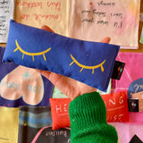 Handmade blue lavender eye bag with yellow closed eyes design held in hand