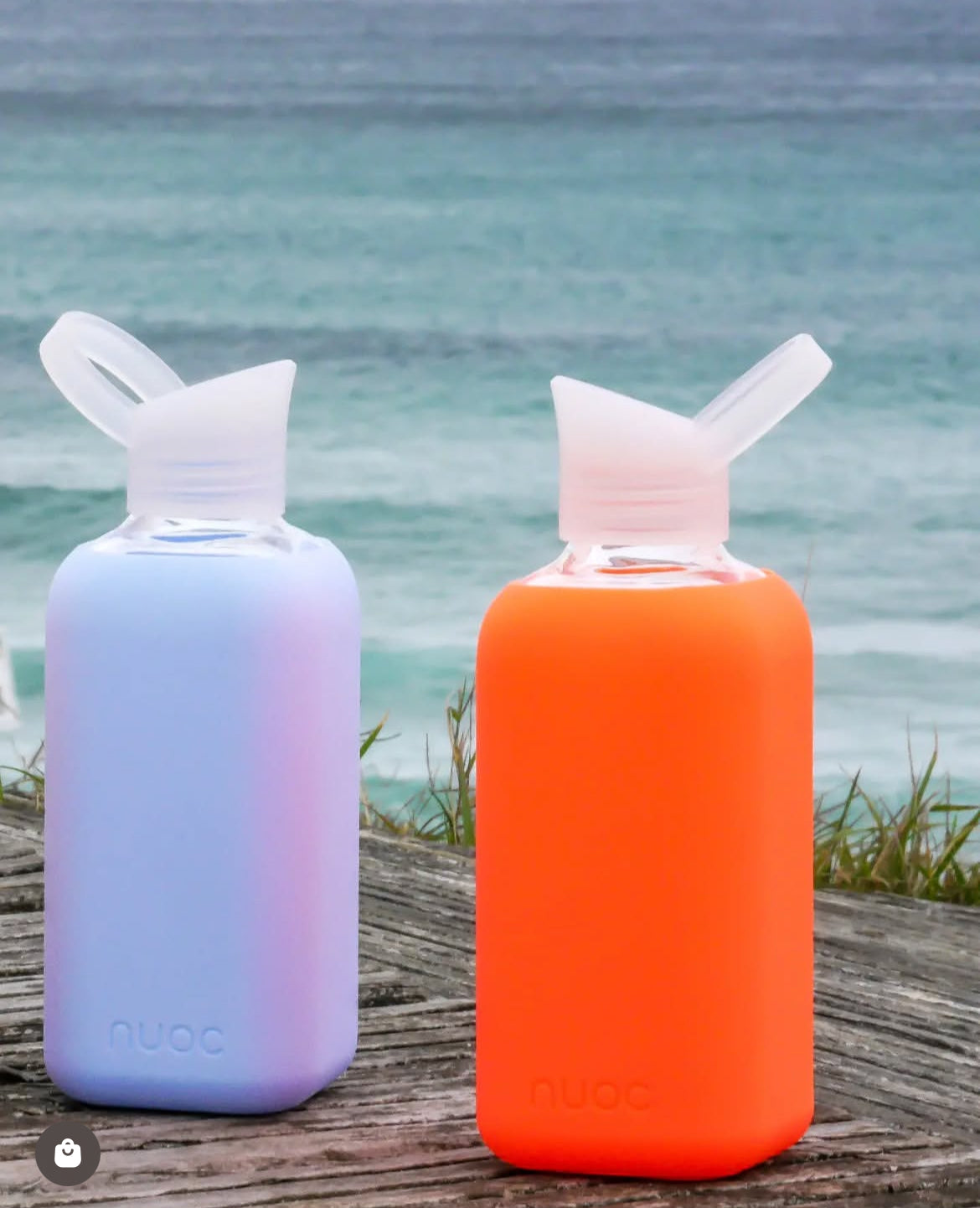Lifestyle photo of NUOC 500ml glass bottles with orange and lavender silicone sleeves, premium reusable swag for sustainable corporate gifting