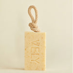 A rectangular bar of VELY soap in a warm cream-beige color with tiny speckles, featuring a knotted natural-fiber loop at the top. The brand name 'VELY' is embossed vertically on the front.