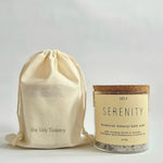 A glass jar of Vely Serenity botanical mineral bath soak with a cork lid and cream label, shown next to a matching cream drawstring pouch printed with 'the Vely Scapery' on a light gray background.