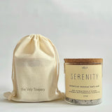 A glass jar of Vely Serenity botanical mineral bath soak with a cork lid and cream label, shown next to a matching cream drawstring pouch printed with 'the Vely Scapery' on a light gray background.