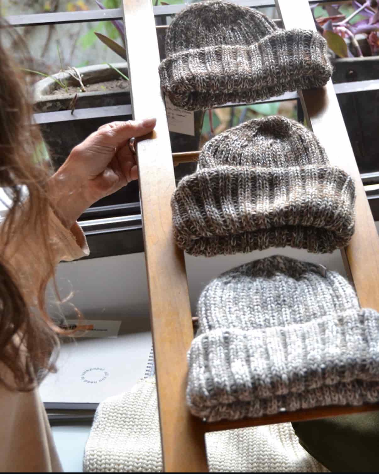 Three hand knitted Fisherman merino wool beanies displayed on a wooden ladder