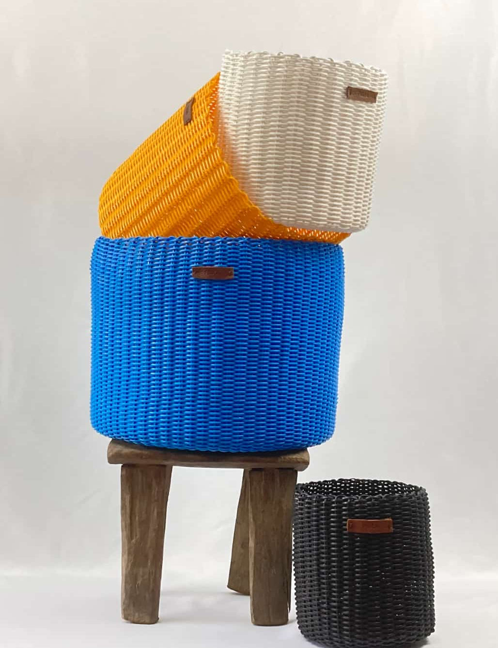 Handwoven upcycled office bins in blue, white, yellow and black, grouped on a stool