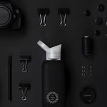 Reusable Glass Bottle 800ml in black, lifestyle shot with other black items, showing logo placement