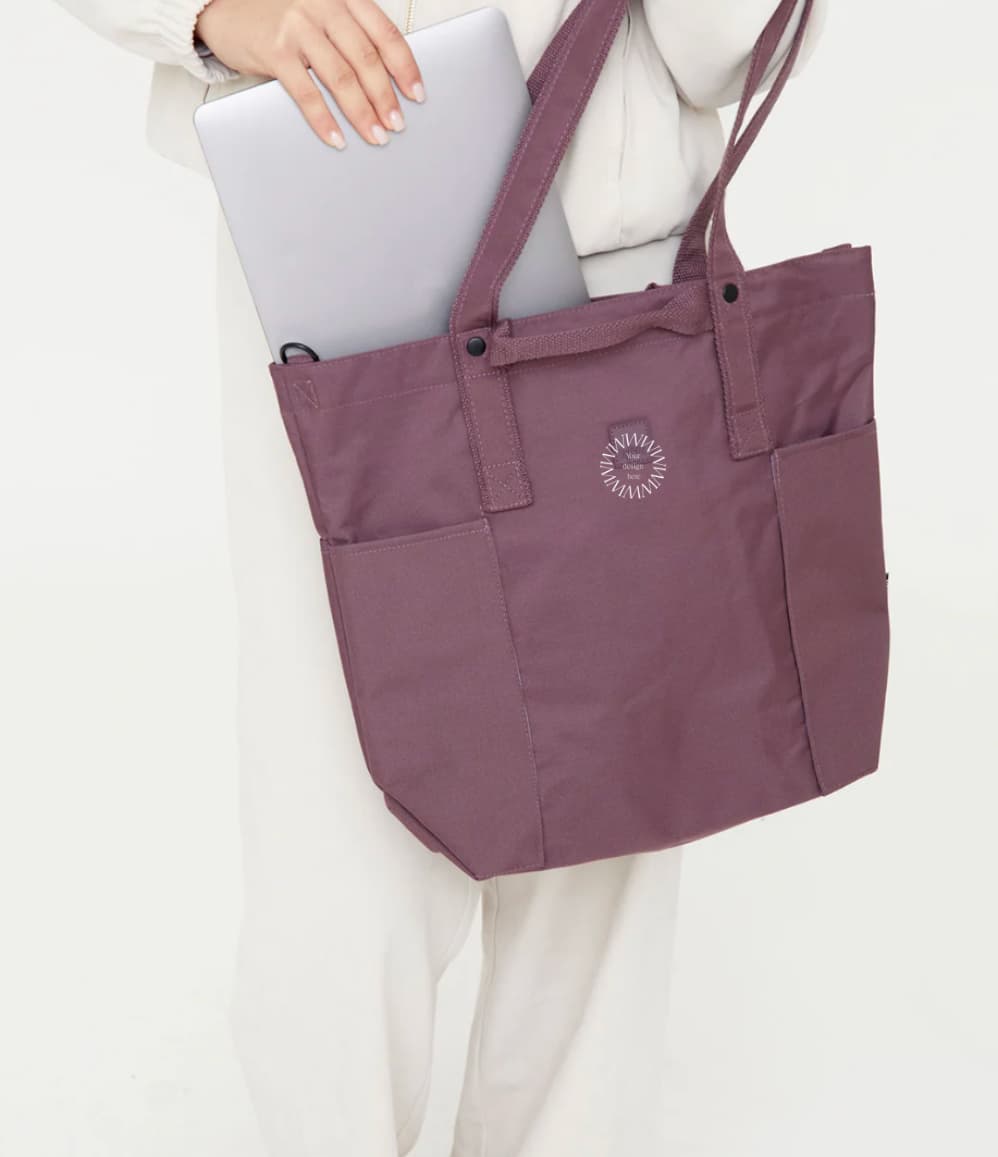 Maroon tote bag with a logo held by a person on a white background