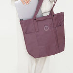 Maroon tote bag with a logo held by a person on a white background
